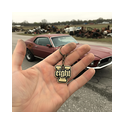 Hand präsentiert einen V8 Eight Schlüsselanhänger aus Messing vor einem US‑Car‑Schrottplatz, ideal für Gearheads, Hot‑Rod‑ und V8‑Fans.