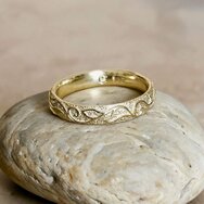 Handgefertigter Trauring aus 585 Gelbgold mit floralem Ornamentmuster auf hellem Naturstein